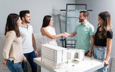 Business partners shaking hands with engineer by architectural model in meeting